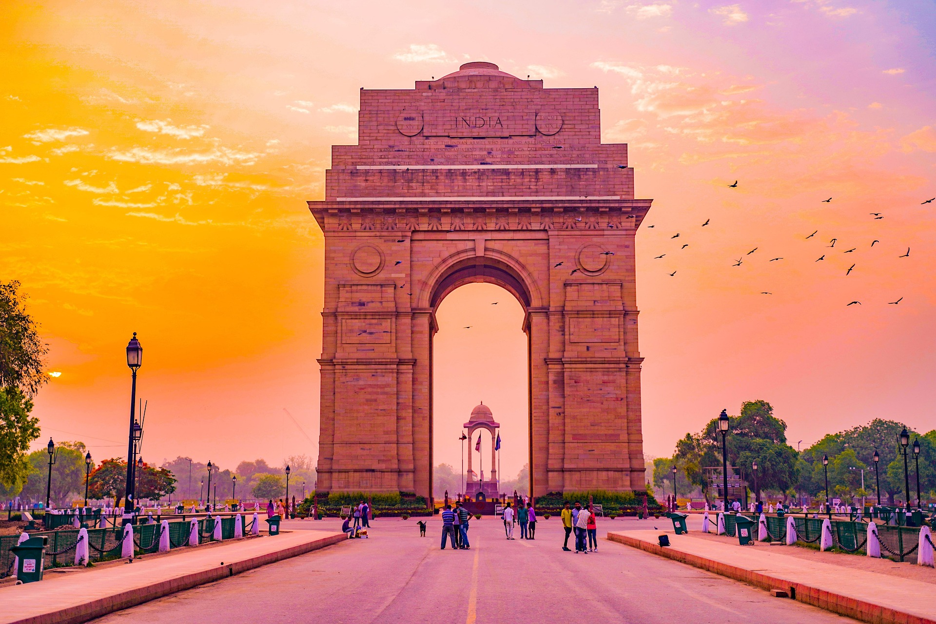 India Gate monument in New Delhi on a clear day with visitors and national flags.